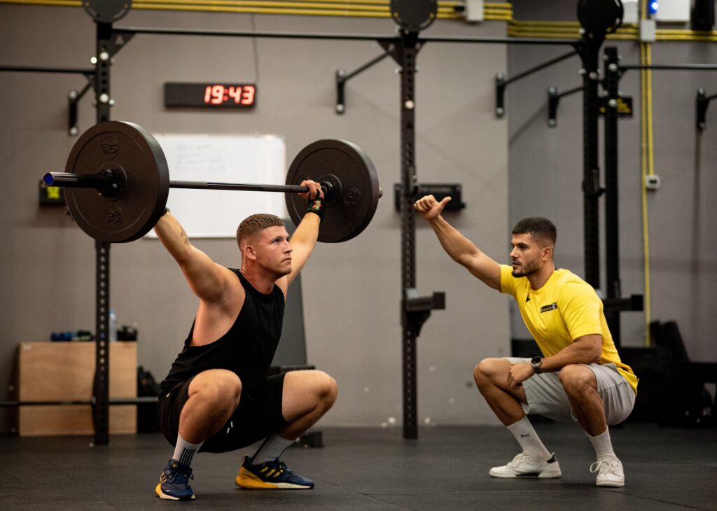 Personal trainer correcting overhead squat technique to improve biomechanics and exercise form.